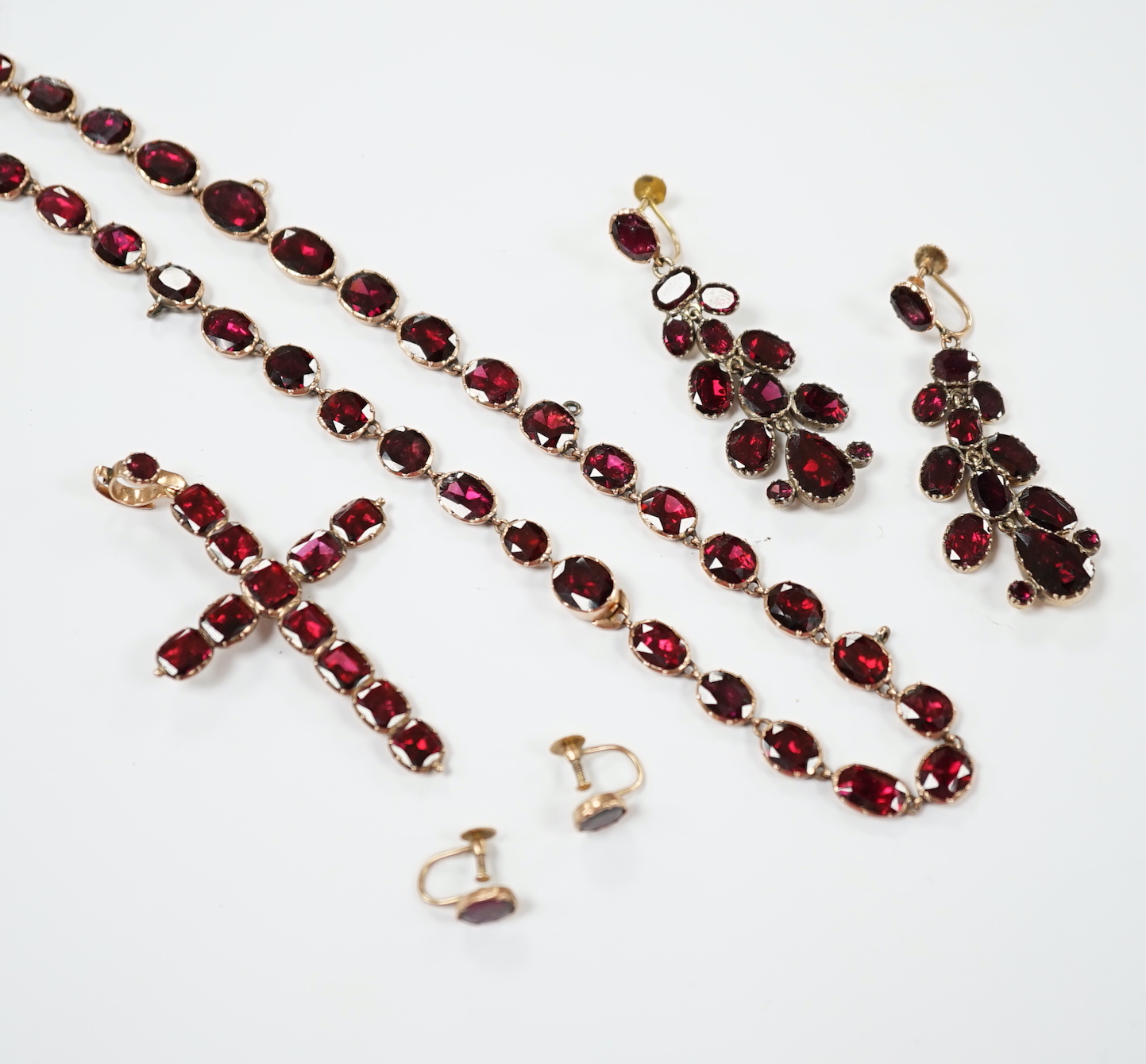 Six items of Victorian oval cut garnet set jewellery, including a yellow metal necklace (lacking drops?), 37cm, a pair of 9ct ear clips, a yellow metal cross pendant with cushion cut stones, gross weight 30 grams and a p